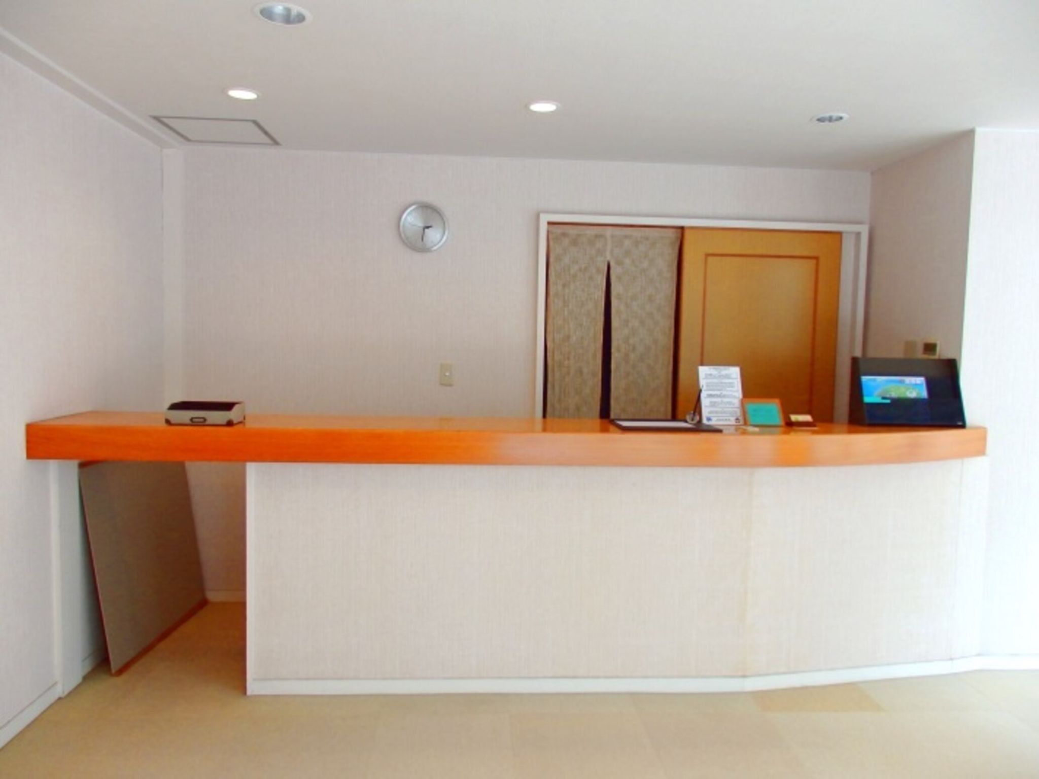 A reception desk with a clock, a door, and a digital screen.