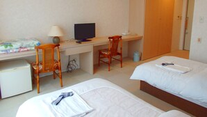 Habitación de hotel con escritorio, computadora, dos sillas, cama y un refrigerador pequeño.