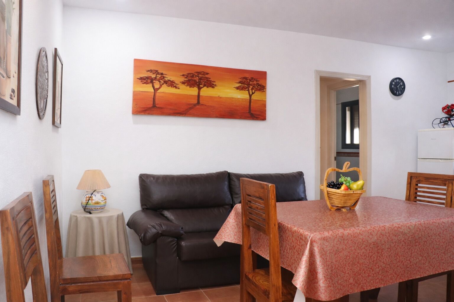 Ein Essbereich mit einem Tisch für zwei Personen, einer Couch, einer Lampe und einem Baumgemälde an der Wand.