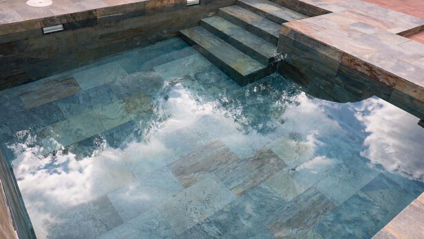 A swimming pool with stone tiles and steps leading into it.