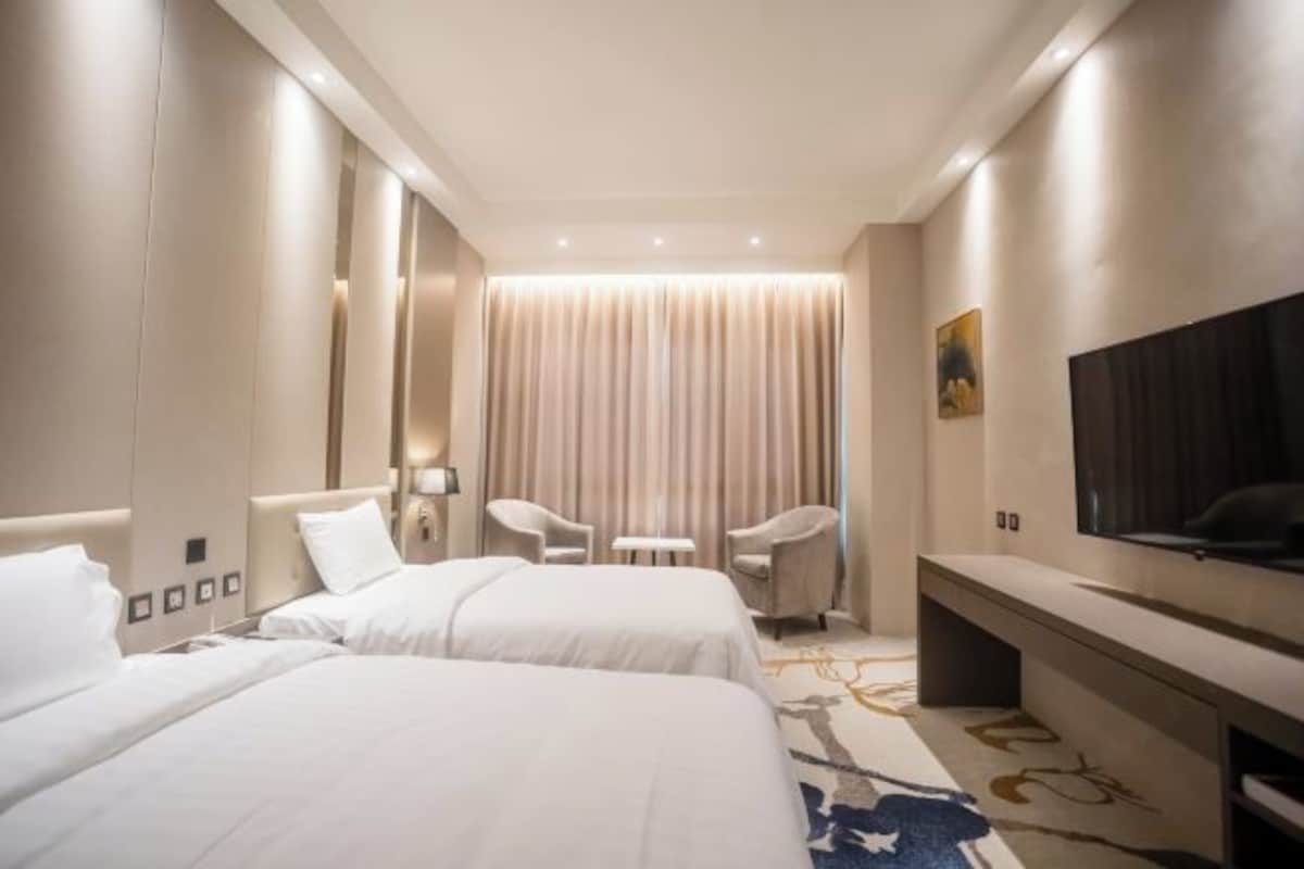 A hotel room with two beds, a TV, a desk, and a chair.