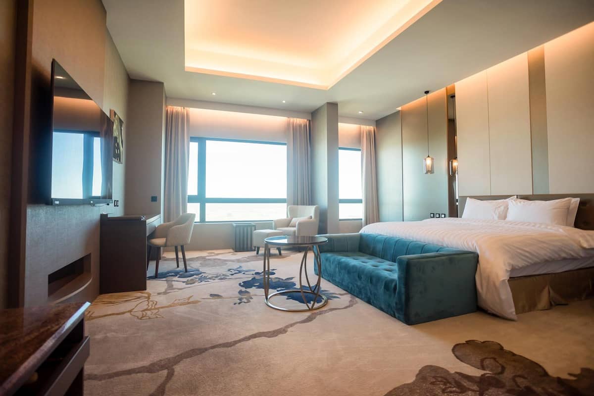Ein Hotelzimmer mit einem großen Bett, einer Sitzecke mit einem kleinen Tisch, einem Fernseher und einem großen Fenster mit Vorhängen.