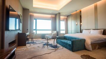 A hotel room with a large bed, a seating area with a small table, a TV, and a large window with curtains.
