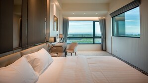 Una habitación de hotel moderna con una cama grande, un escritorio, una silla y vistas a la ciudad a través de amplios ventanales.