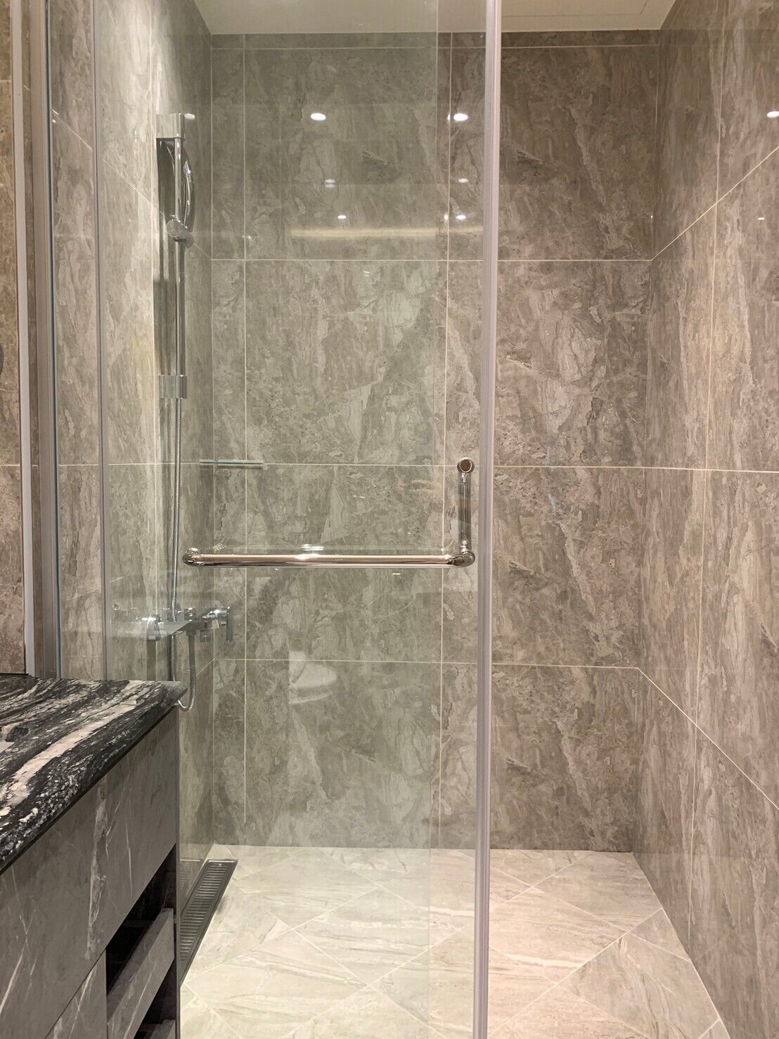 Une salle de bain moderne dotée d’une douche à parois de verre, de carreaux de marbre et d’un comptoir en granit.