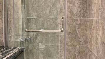 A modern bathroom with a glass-enclosed shower, marble tiles, and a granite countertop.