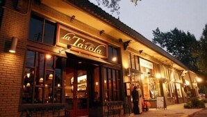 ”La Tavola” -niminen ravintola, jossa on ulkoterasseja ja tiiliverhoiltu julkisivu.