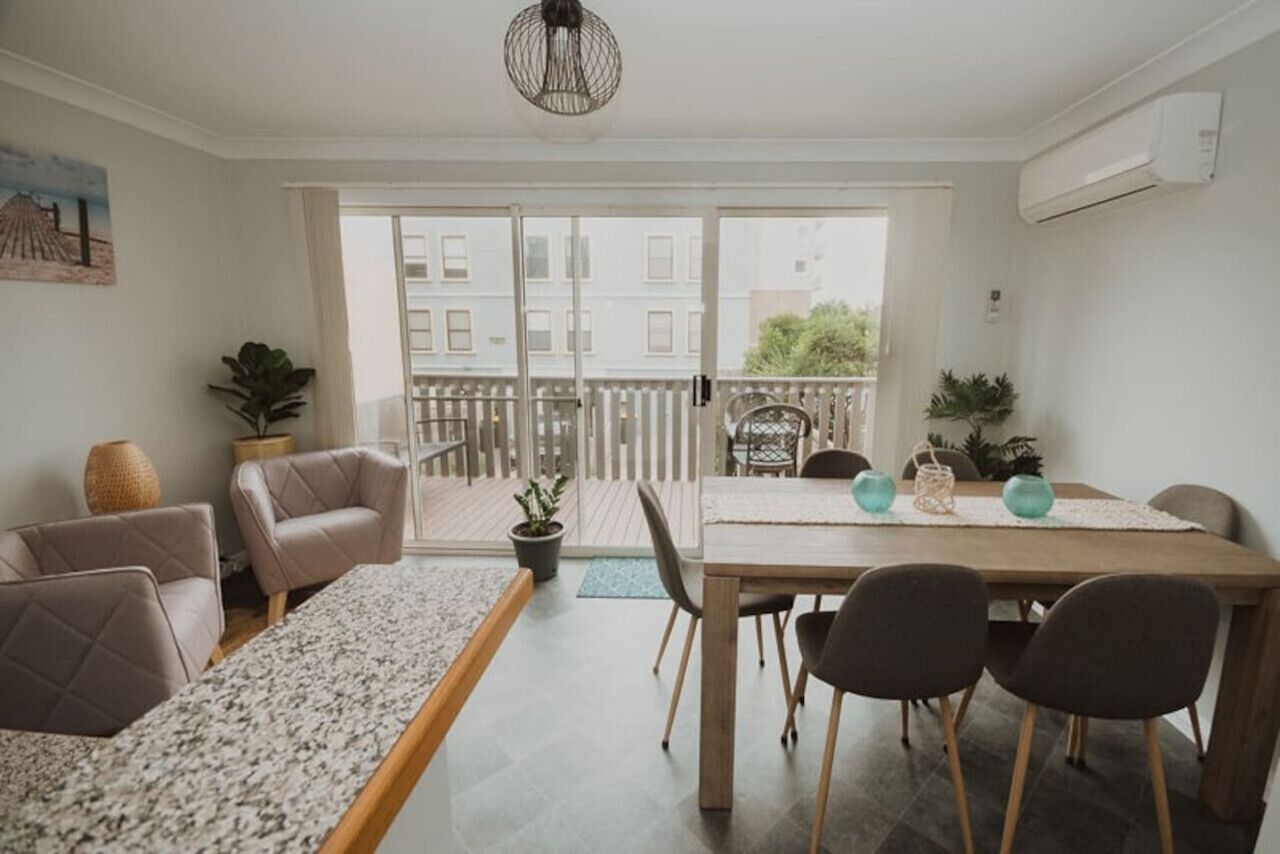 A modern living room with a dining area, a balcony with a wooden railing, and a view of the cityscape.