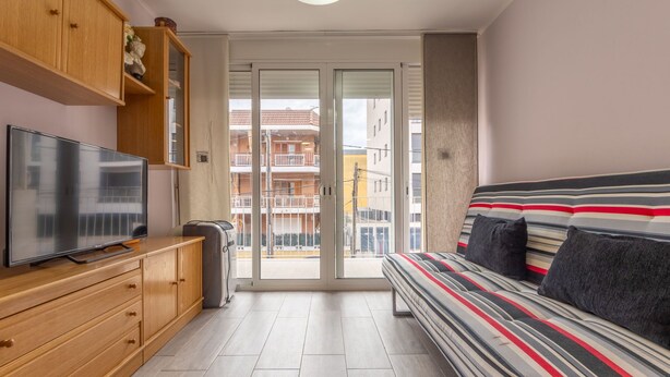 A modern bedroom with a large bed, wooden furniture, a television, and a sliding glass door to a balcony. - Apartment Alda by Interhome (Segur de Calafell)