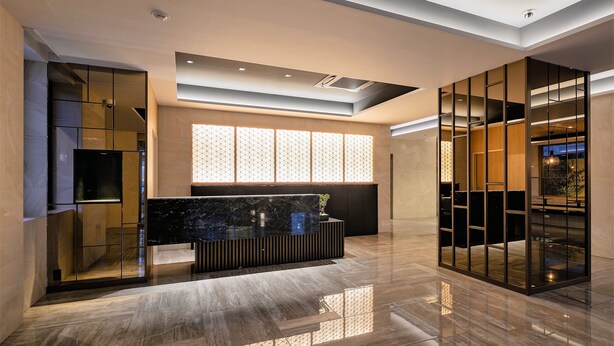 Un vestíbulo moderno con un mostrador de recepción negro, un ventanal con persianas decorativas y un piso pulido.