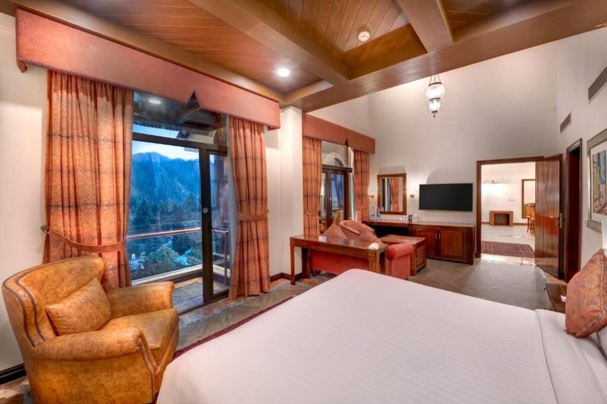 A bedroom with a large bed, a desk, a chair, and a TV.