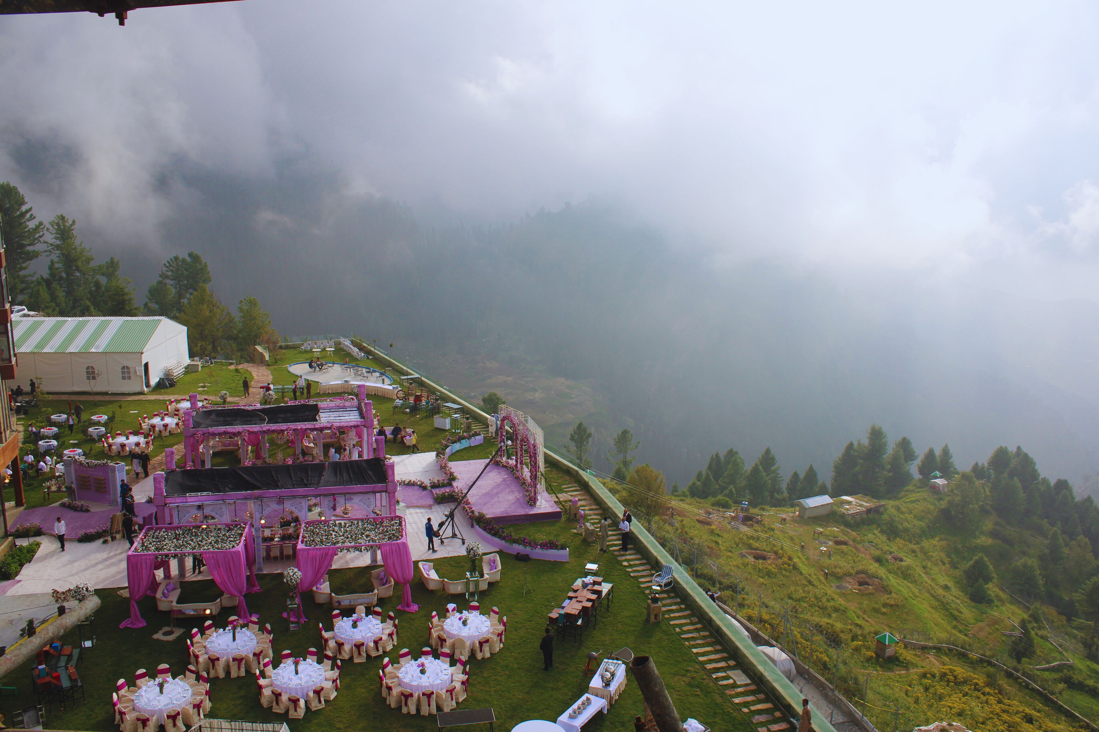 A wedding venue with multiple round tables, a stage, and a scenic mountainous backdrop.