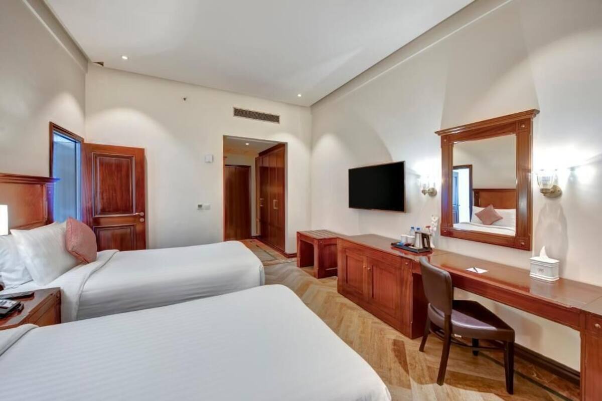 A hotel room with two beds, a desk, a chair, a TV, and a large mirror.