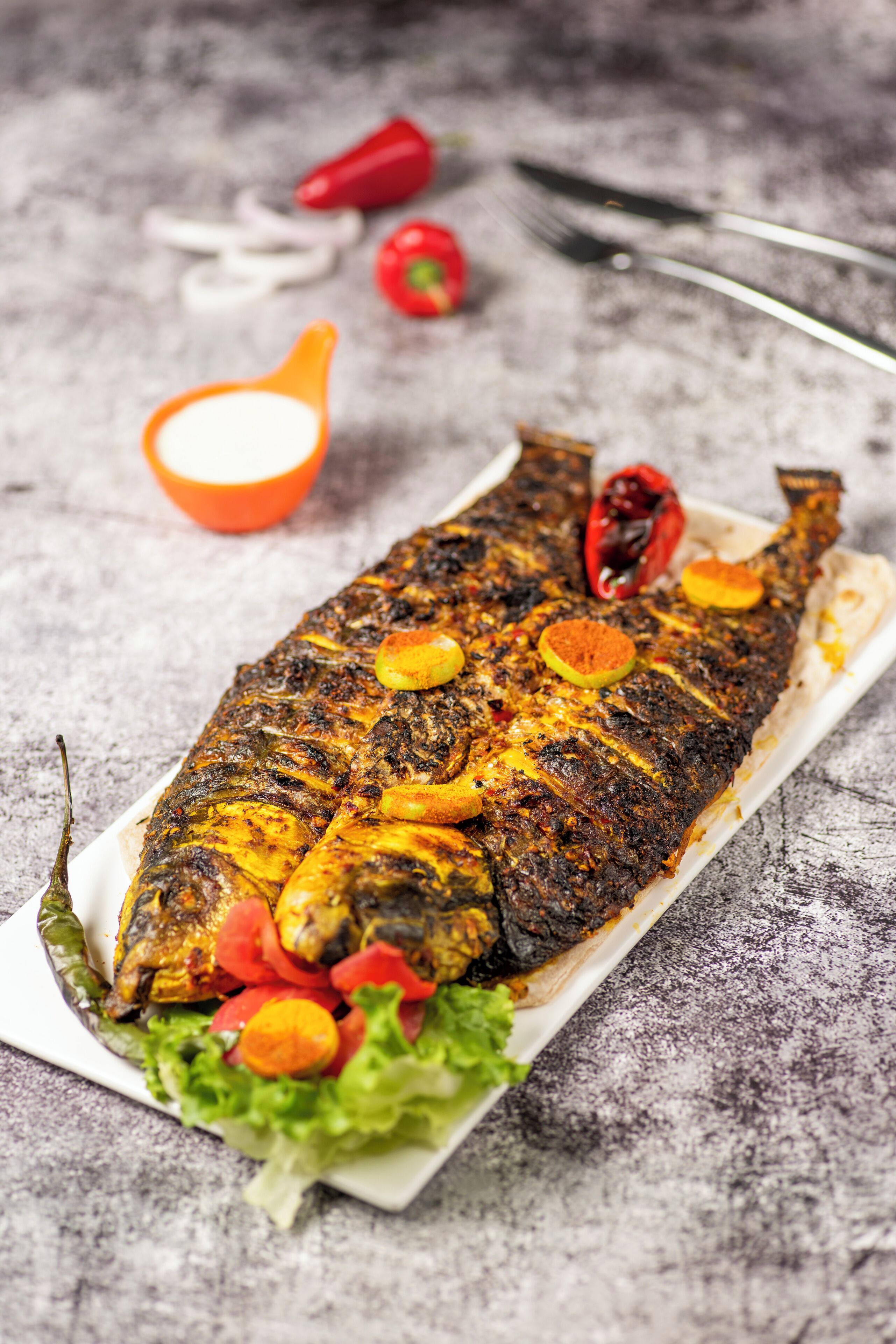 A grilled fish with vegetables on a white plate.
