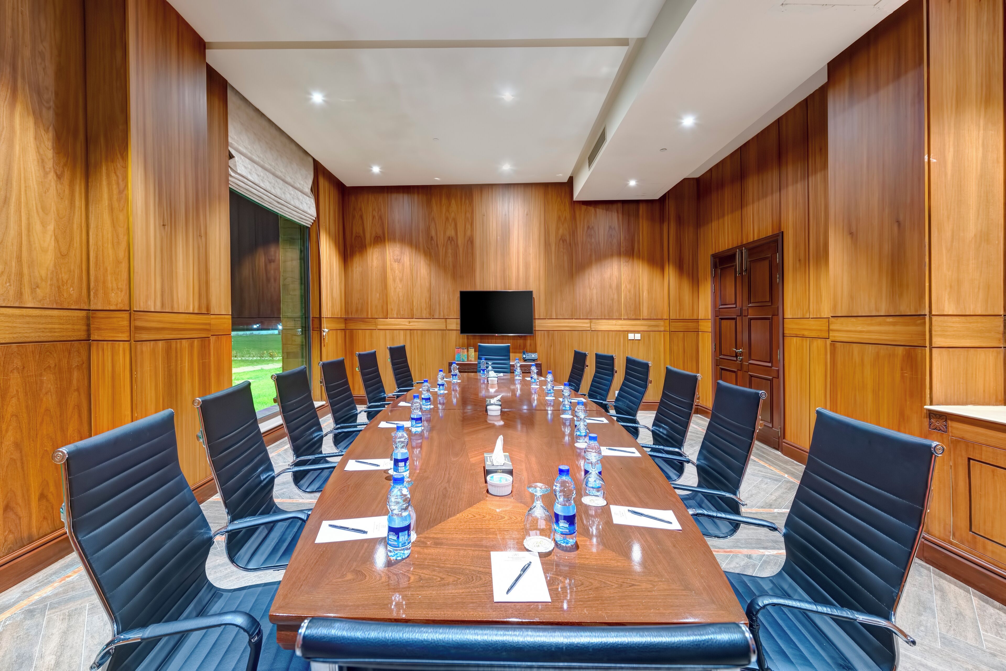 A conference room with a long wooden table, black chairs, and a flat-screen TV.