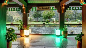 A covered area with a sign reading "Front Page Cafe," potted plants, and a view of a park and water body. - Pearl Continental Hotel Malam Jabba (Swat)