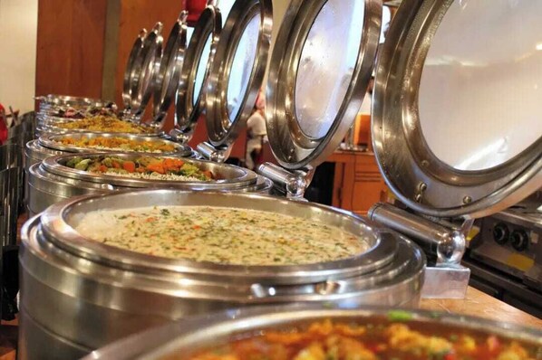 Una barra de buffet con diversos platos en recipientes de acero inoxidable.