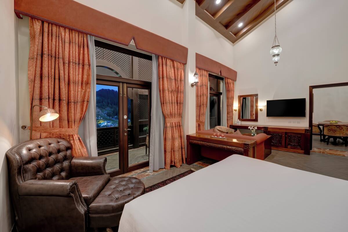 A hotel room with a large bed, leather armchair, and a dining area with a table and chairs.