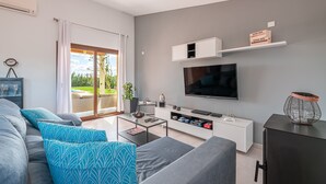 A modern living room with a sofa, coffee table, TV, and a balcony with a sliding door. - Holiday Home “El Rafal de Son Alberti” with Mountain View, Air Conditioning and Pool (Buger)