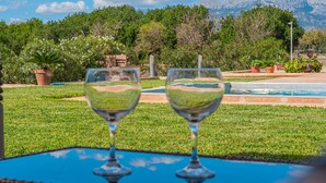 Two wine glasses on a table with a view of a pool and mountains in the background. - Holiday Home “El Rafal de Son Alberti” with Mountain View, Air Conditioning and Pool (Buger)
