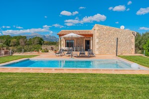 Un edificio de piedra con piscina, mobiliario exterior y vistas a la montaña.