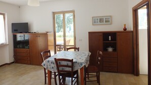 A dining area with a table, chairs, a television on a cabinet, and a door leading outside.