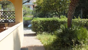 A balcony with a view of a garden, a pathway, and a building in the background.