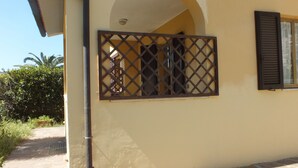 A building with a yellow exterior, a visible window with shutters, and a metal gate.