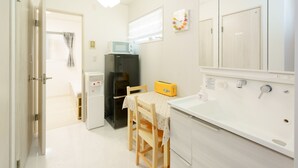 A compact kitchen with a microwave, refrigerator, and a table with a chair. - osaka yeon house (Osaka)