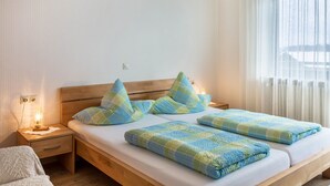 A bedroom with a wooden bed, a nightstand with a lamp, and a window with curtains.