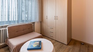 A bedroom with a bed, a bedside table with a book, a wardrobe, and a window with curtains.