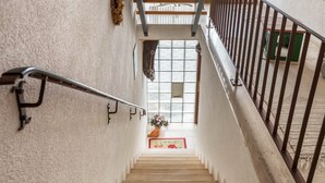 A staircase with a handrail, a window with curtains, and a red mat at the bottom.