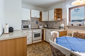Une cuisine compacte avec des meubles blancs, un four à micro-ondes, une cuisinière et un coin repas comprenant une table et des chaises.