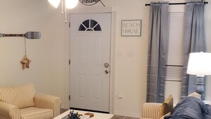 A living room with striped sofas, a coffee table with decorative items, a ceiling fan, and a door with a 'Welcome' sign.