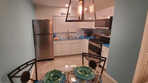 A compact kitchen with a refrigerator, stove, and sink. There is a dining table with chairs and a decorative glass bowl.
