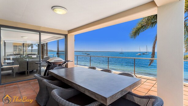 Un balcón con vista al mar, muebles de mimbre y una mesa.