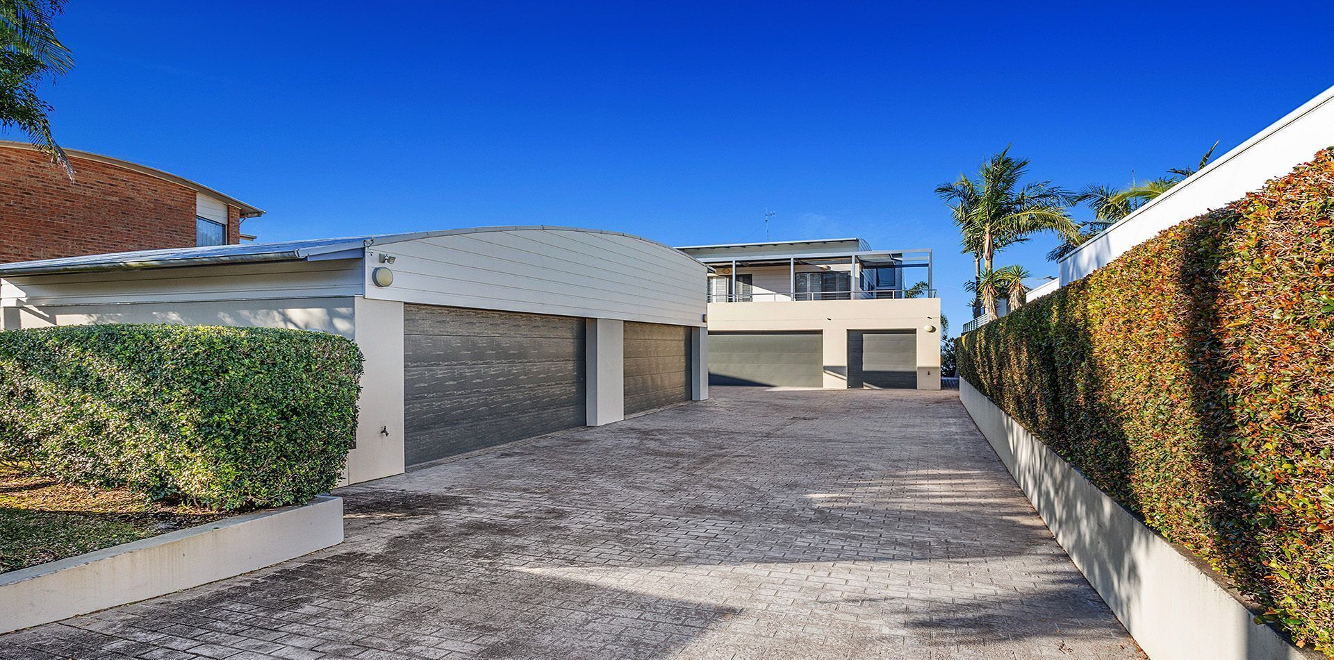 A modern residential building with a covered driveway, a garage, and a well-maintained hedge.