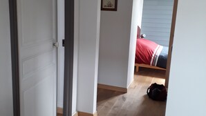 A hallway with a wooden floor leading to a bedroom with a bed and a red bag on the floor. - Duplex apartment with sea view (Saint-Cast-le-Guildo)