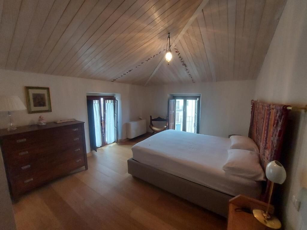 Un dormitorio con una cama grande, un aparador, una silla y un escritorio. Hay una ventana y una puerta.