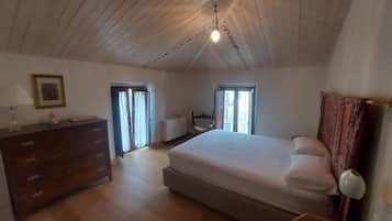 Un dormitorio con una cama grande, un aparador, una silla y un escritorio. Hay una ventana y una puerta.