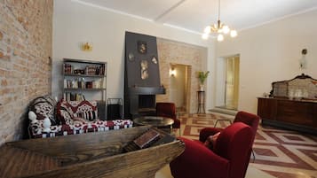 A living room with a fireplace, red armchairs, a wooden coffee table, and a bookshelf.
