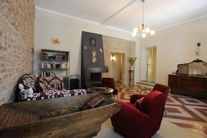Een woonkamer met een open haard, rode fauteuils, een houten salontafel en een boekenkast.