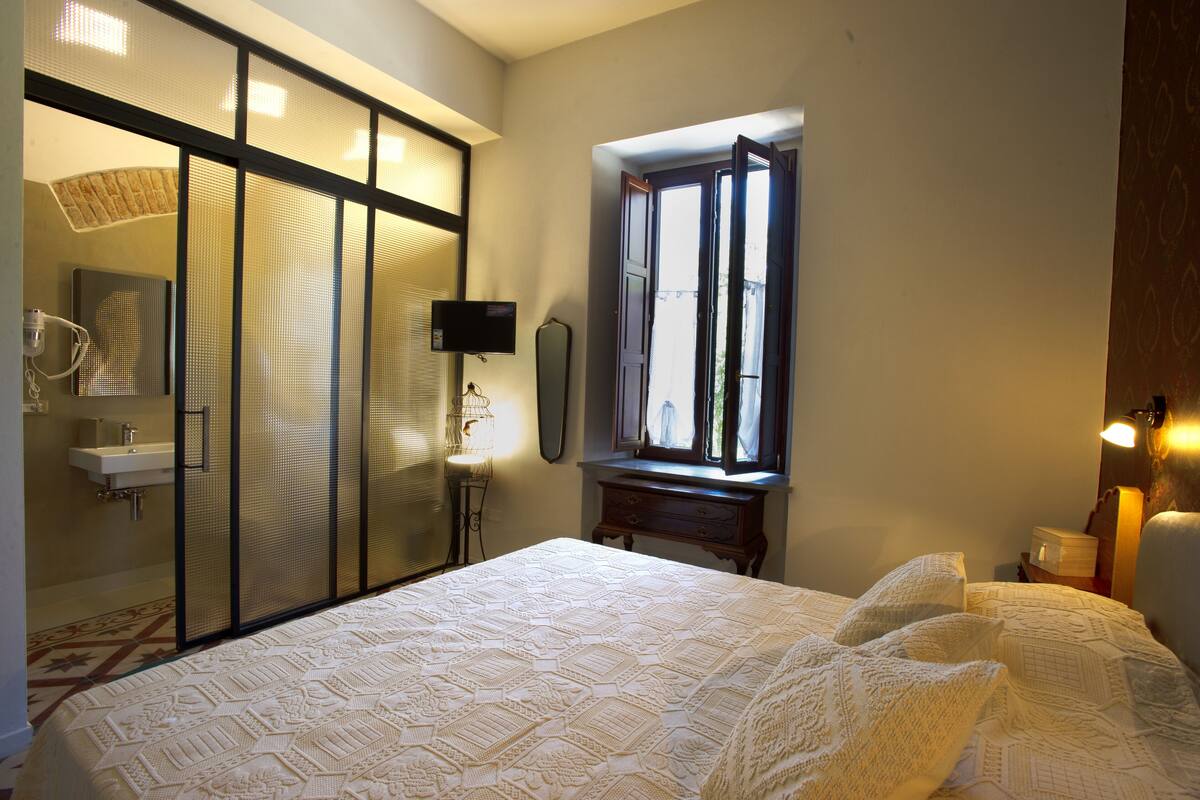 Ein Schlafzimmer mit einem großen Bett, einem Fenster mit Blick, einem Nachttisch und einem Spiegel.
