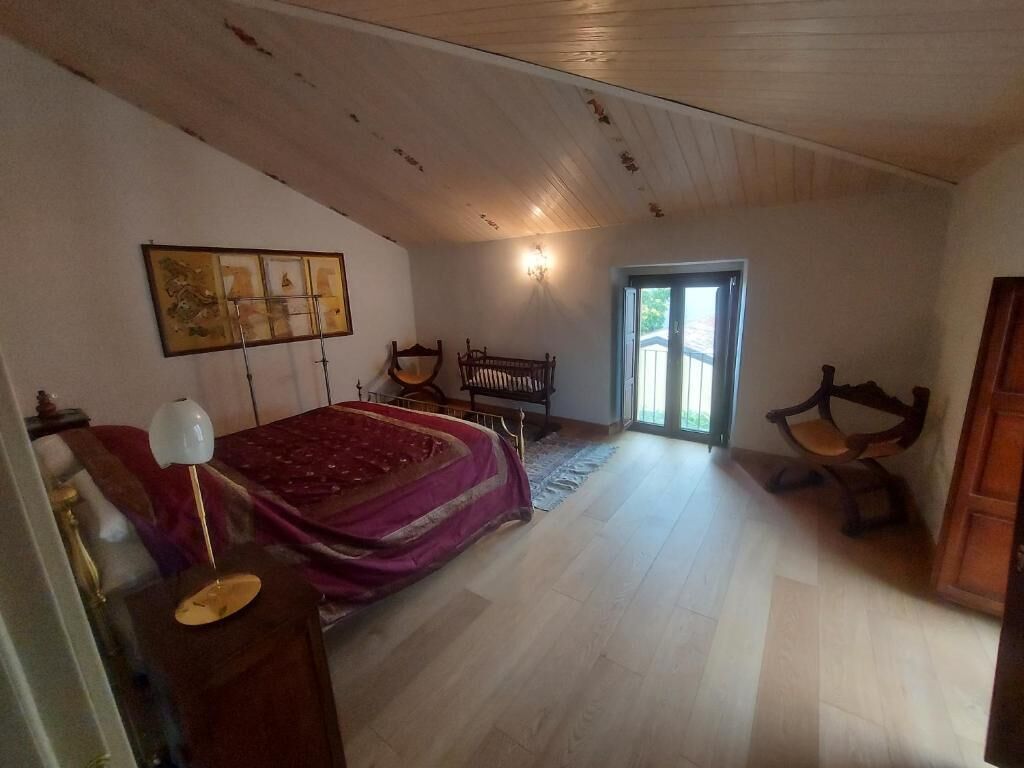 Een slaapkamer met een bed, nachtkastje, lamp, stoel, bankje en een deur naar een balkon.