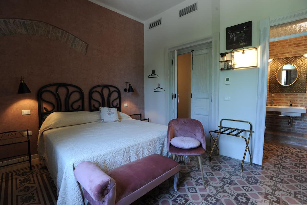 Ein Schlafzimmer mit Bett, Stuhl, Sitzbank und Kleiderschrank, sowie ein Badezimmer mit Waschbecken und Spiegel.