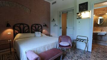 Quarto com cama, poltrona, banqueta, guarda-roupa e banheiro com pia e espelho.
