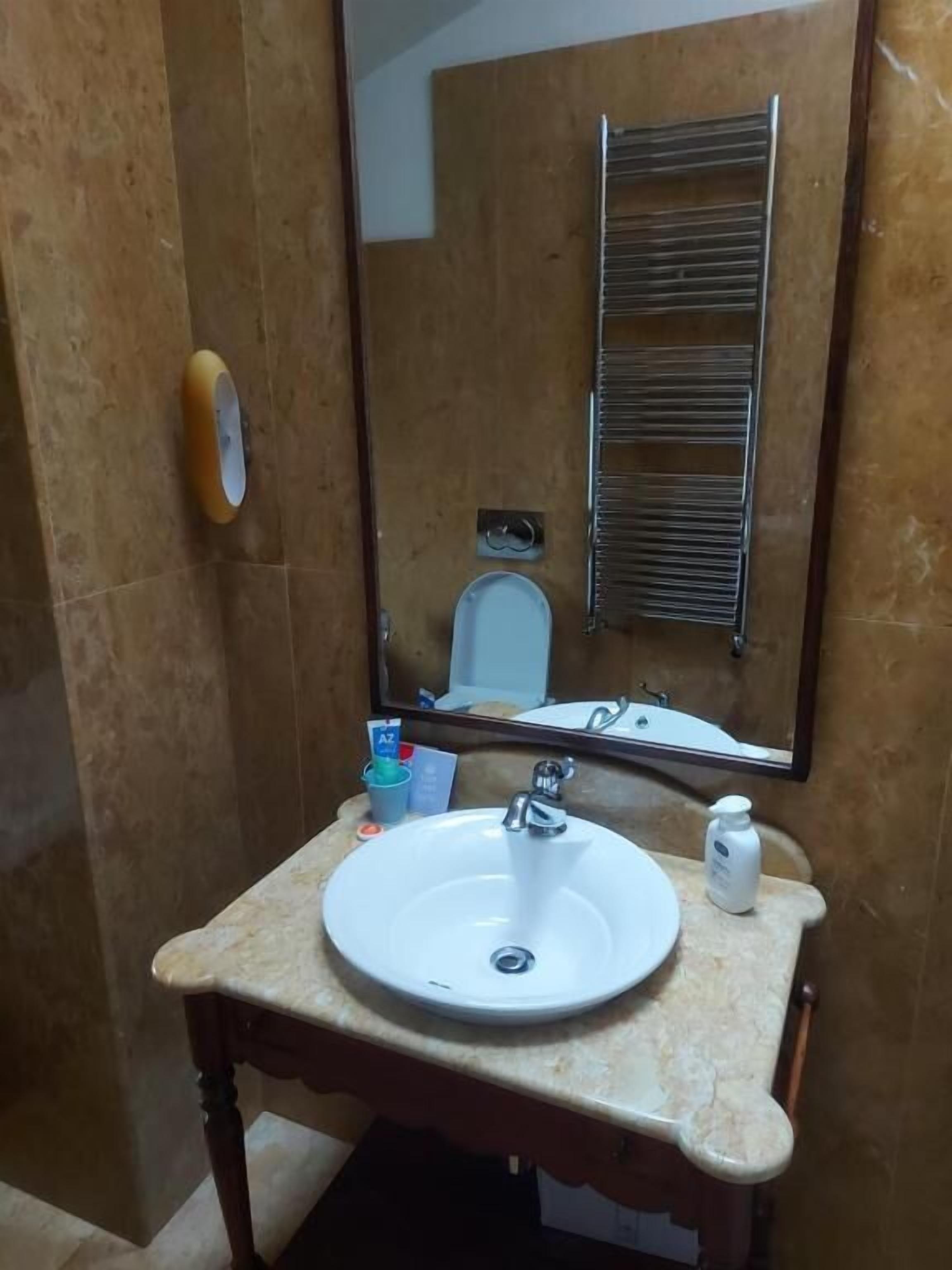 A bathroom with a sink, mirror, towel rack, and a small bottle on the countertop.