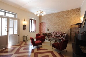 Un salon avec un mur en briques, un canapé, des fauteuils rouges et une cheminée.