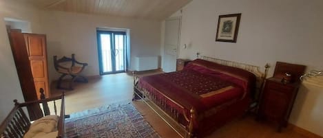 A bedroom with a large bed, a wooden chair, a rug, and a door leading to another room.