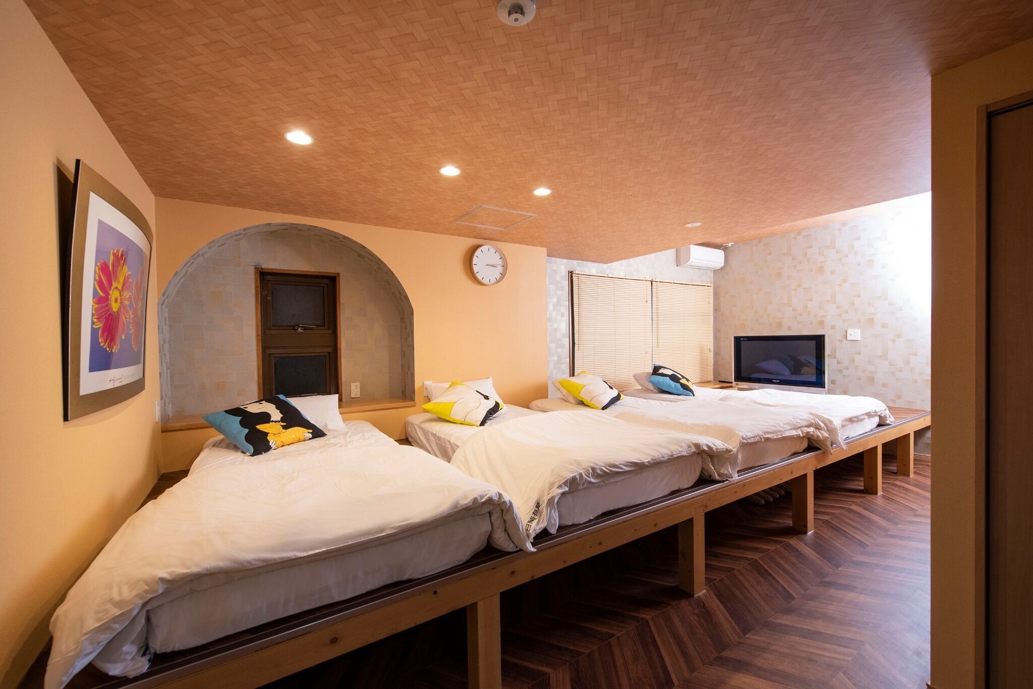 Una habitación con tres camas, un reloj, un televisor y un cuadro en la pared.